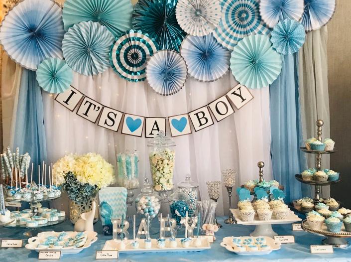 Sweet as can be little baby boy elephant, blue, white and silver themed baby shower dessert table with pinwheel fans and draped photo backdrop. Showcasing an array of desserts; candy jars, meringue kisses, cupcakes, cake pops, chocolate covered Oreo's and chocolate covered pretzel rods