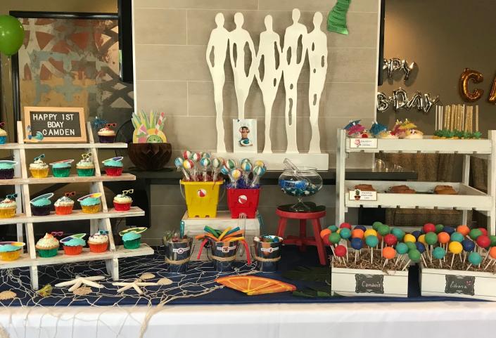 A beachy vibe for a one year old Pool party, Cabana themed birthday party dessert table. Surf board cupcakes, beach ball cake pops, mini upside down pineapple cakes and pina colada cupcakes! 